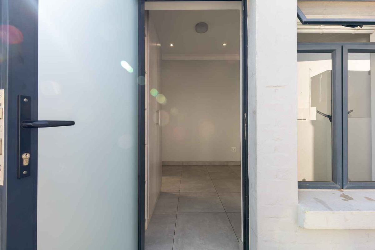 A view through an open doorway into a clean, empty bedroom featuring tiled floors, built-in cupboards, and modern recessed lighting.