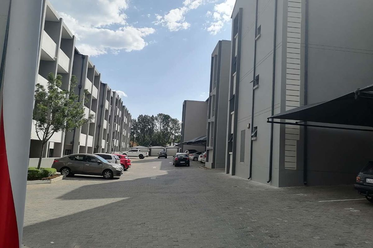 Exterior view of a modern apartment complex featuring paved parking areas and multi-story residential buildings with contemporary grey facades.
