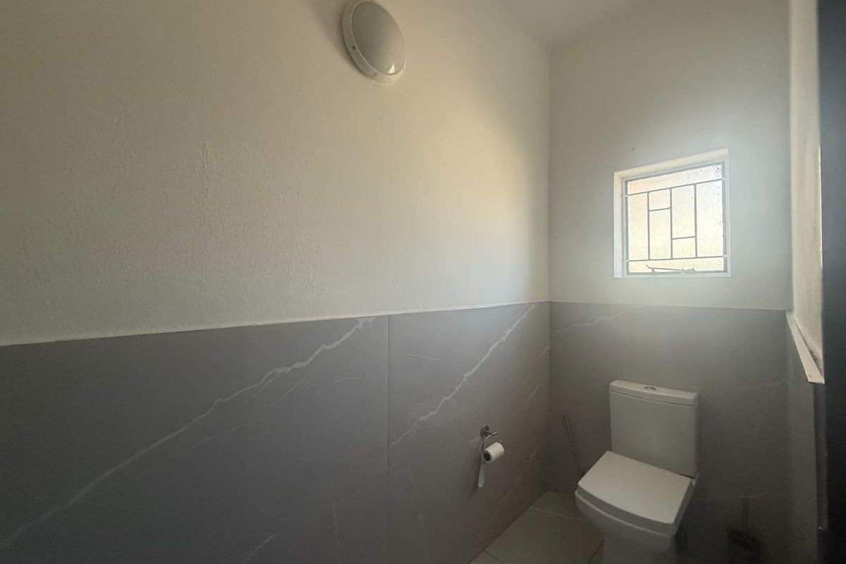 A clean and functional bathroom featuring modern grey wall tiles, a white toilet, and a small window with security bars.