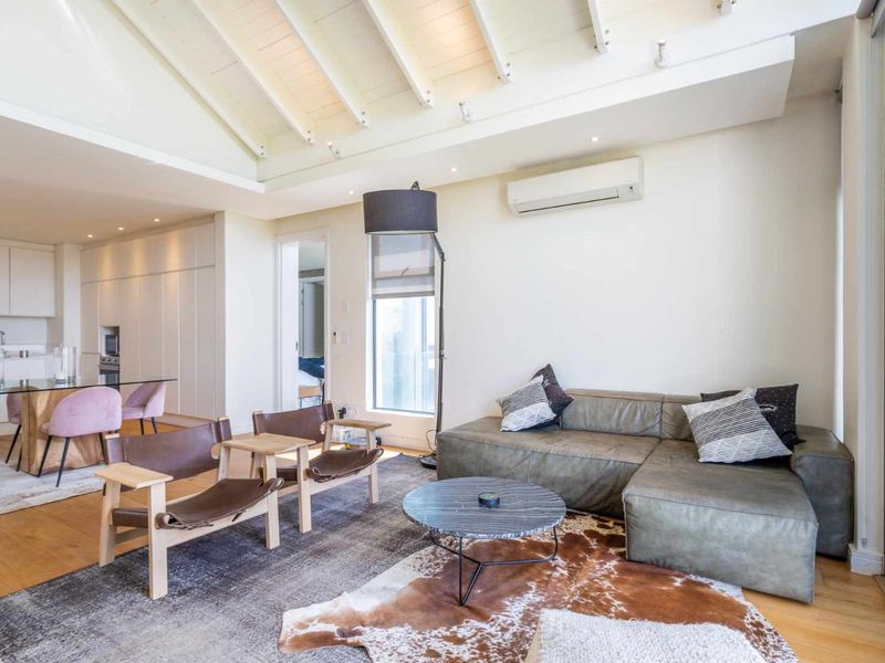 Spacious open-plan living and dining area featuring vaulted ceilings with exposed rafters, hardwood flooring, and integrated kitchen cabinetry.