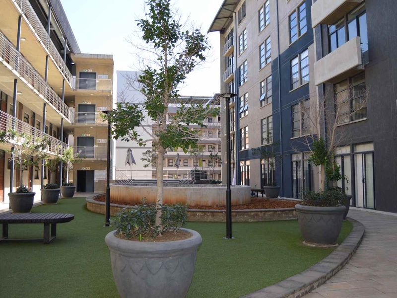 A communal courtyard area between apartment blocks featuring artificial turf, paved walkways, and a central concrete planter.