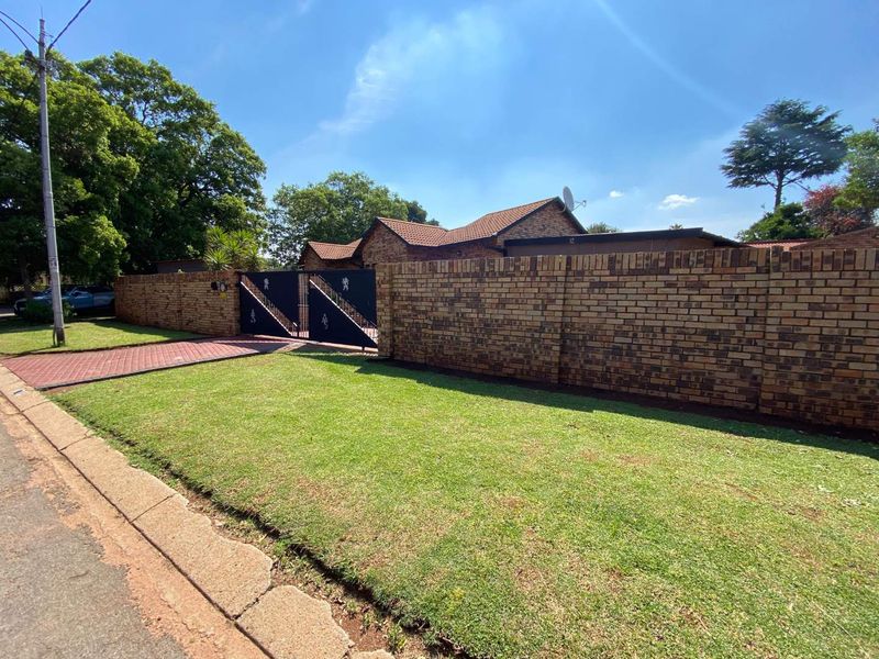 Front view of the property featuring a brick boundary wall, secure metal driveway gate, paved driveway, and a well-maintained lawn.