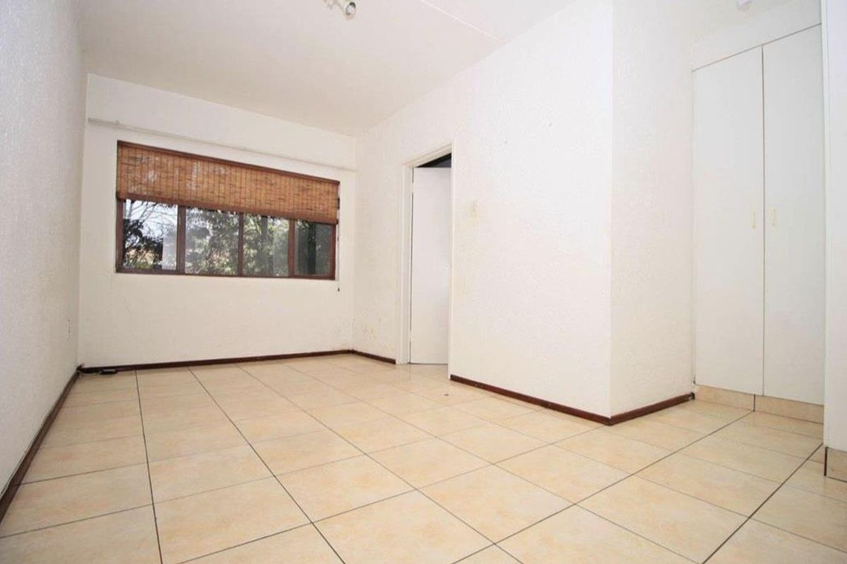 An empty bedroom featuring tiled flooring, built-in cupboards, and a window with a bamboo blind, offering a neutral space ready for personalization.