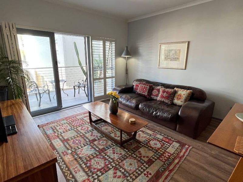 A comfortable living room featuring laminate flooring, track lighting, and a large sliding glass door providing access to a private balcony.