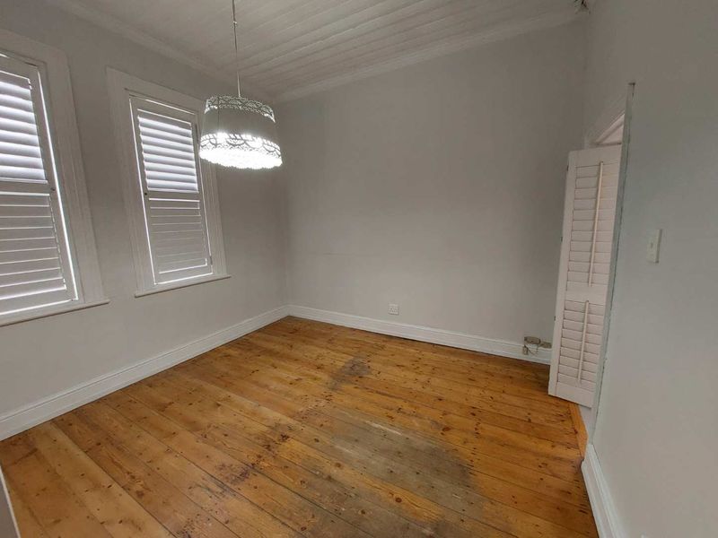 An empty bedroom featuring original timber flooring, plantation shutters, and a classic tongue and groove ceiling.