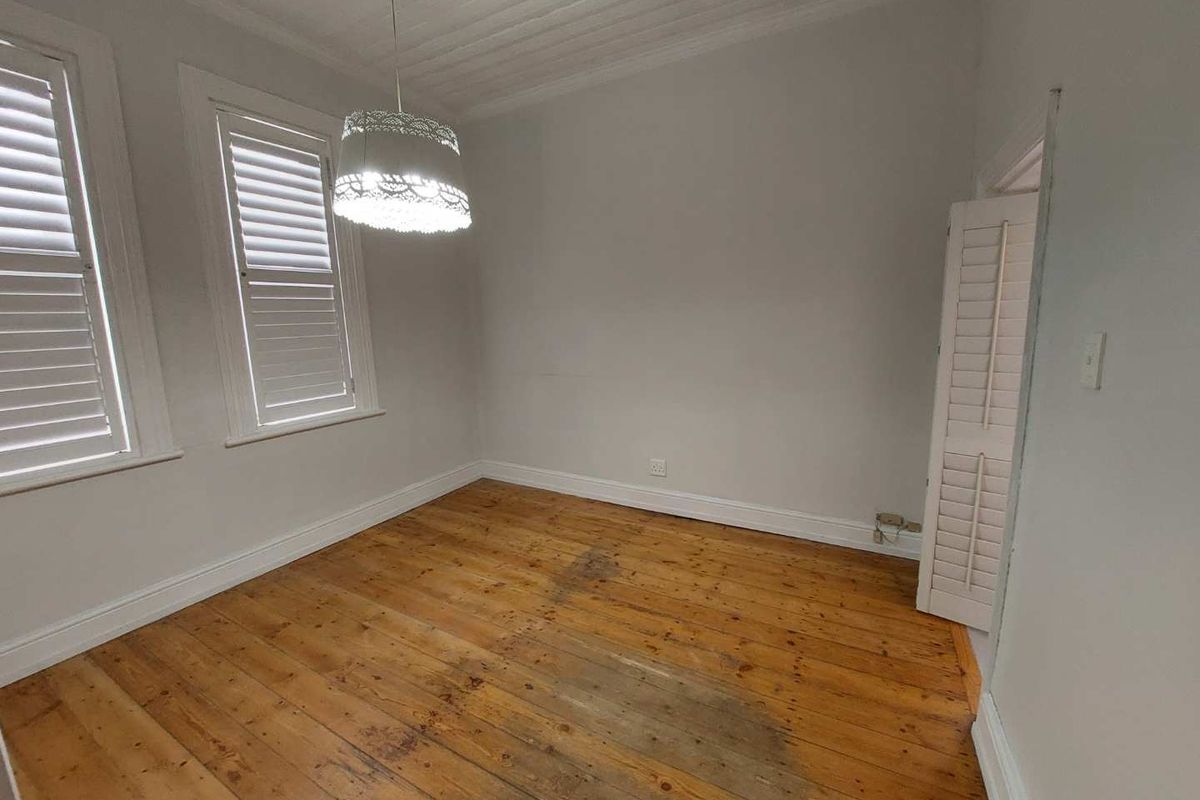 An empty bedroom featuring original timber flooring, plantation shutters, and a classic tongue and groove ceiling.