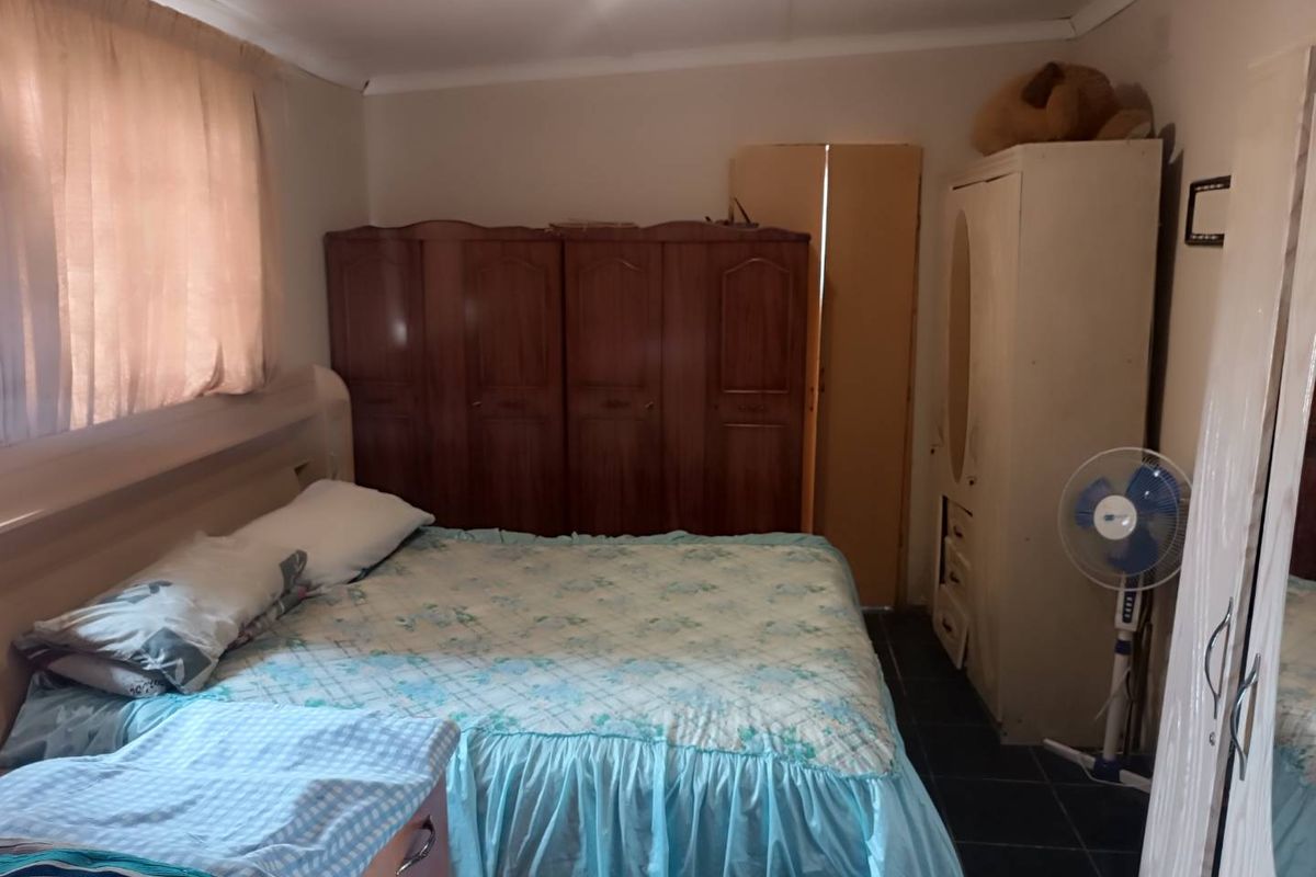 A functional bedroom featuring tiled flooring, built-in wooden cabinetry, and a window with curtain treatments.