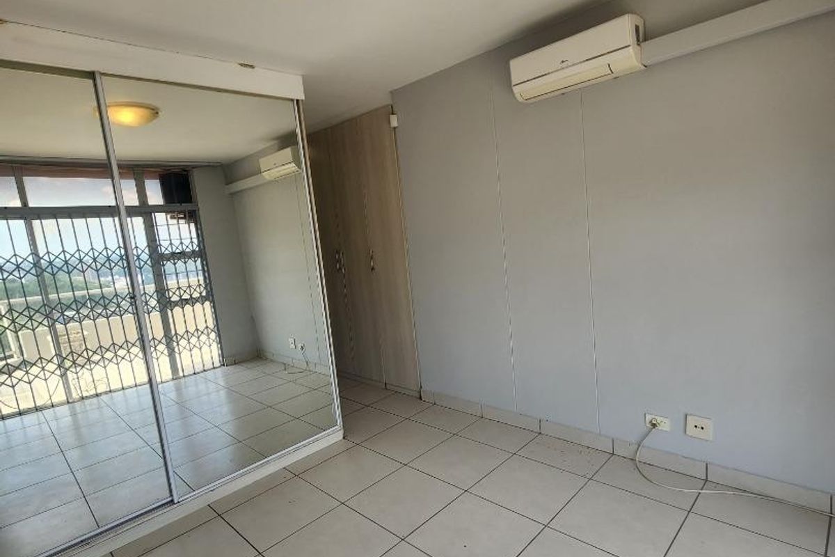 A bright, empty bedroom featuring tiled flooring, a large mirrored sliding wardrobe, and a wall-mounted split-system air conditioner.