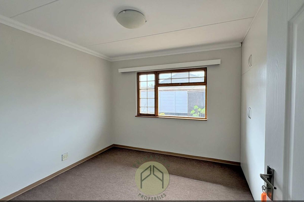 A clean, empty bedroom featuring neutral walls, carpeted flooring, and built-in storage cupboards.
