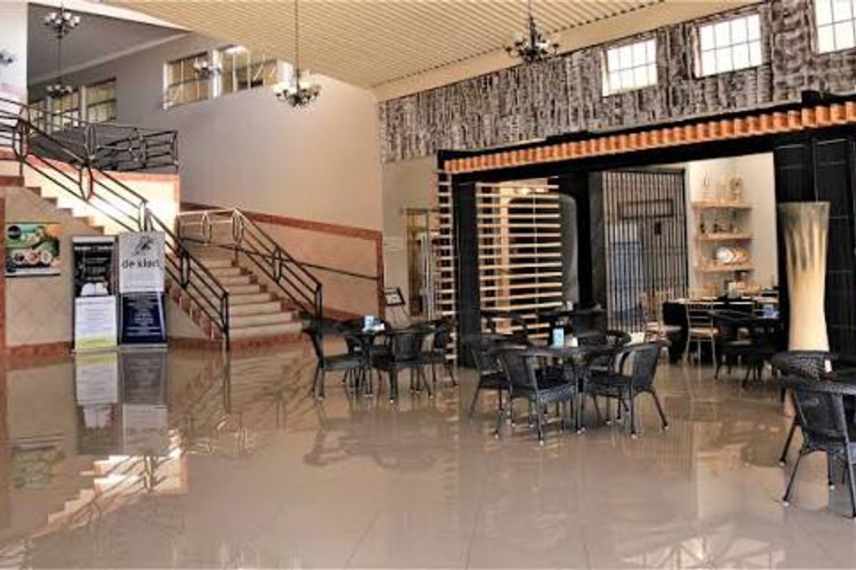 Spacious open-plan commercial interior featuring a grand staircase, tiled flooring, and integrated dining area with modern lighting and architectural metalwork.