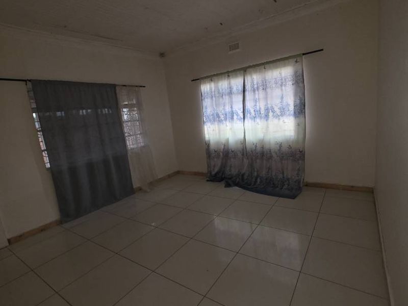 An empty living room featuring tiled flooring and a timber plank ceiling, offering a blank canvas for renovation and interior design.