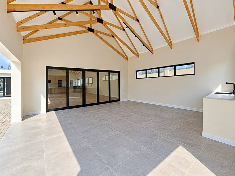Spacious covered patio featuring exposed timber trusses, large format floor tiles, built-in sink, and black aluminium sliding doors leading to the interior living area.