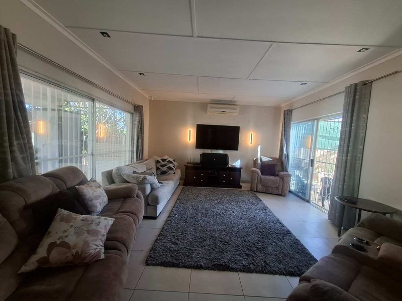 Spacious living room featuring tiled flooring, recessed ceiling lighting, a wall-mounted air conditioner, and large sliding glass doors providing access to the exterior.