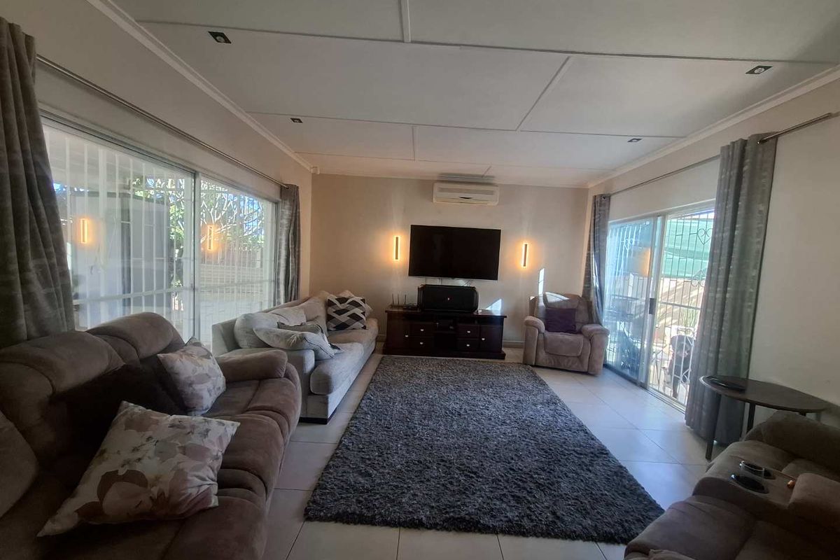 Spacious living room featuring tiled flooring, recessed ceiling lighting, a wall-mounted air conditioner, and large sliding glass doors providing access to the exterior.