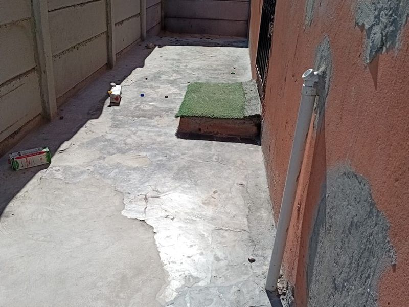 A narrow rear exterior area featuring a precast concrete boundary wall and weathered concrete paving with visible surface damage and wall repairs.