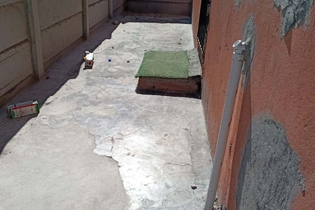 A narrow rear exterior area featuring a precast concrete boundary wall and weathered concrete paving with visible surface damage and wall repairs.