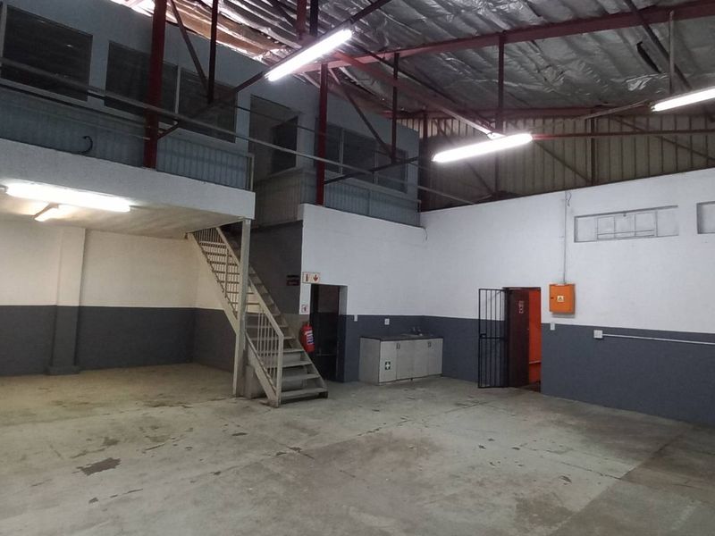 Spacious industrial utility area featuring a mezzanine level, metal staircase, exposed roof trusses, and a small kitchenette unit, suitable for workshop or storage use.