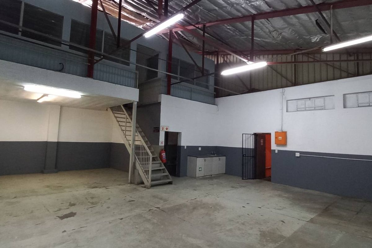 Spacious industrial utility area featuring a mezzanine level, metal staircase, exposed roof trusses, and a small kitchenette unit, suitable for workshop or storage use.