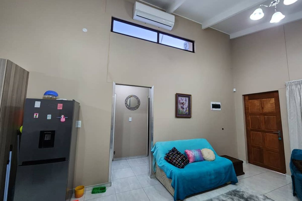 Spacious living area featuring high vaulted ceilings, tiled flooring, a wall-mounted air conditioning unit, and clerestory windows for natural light.