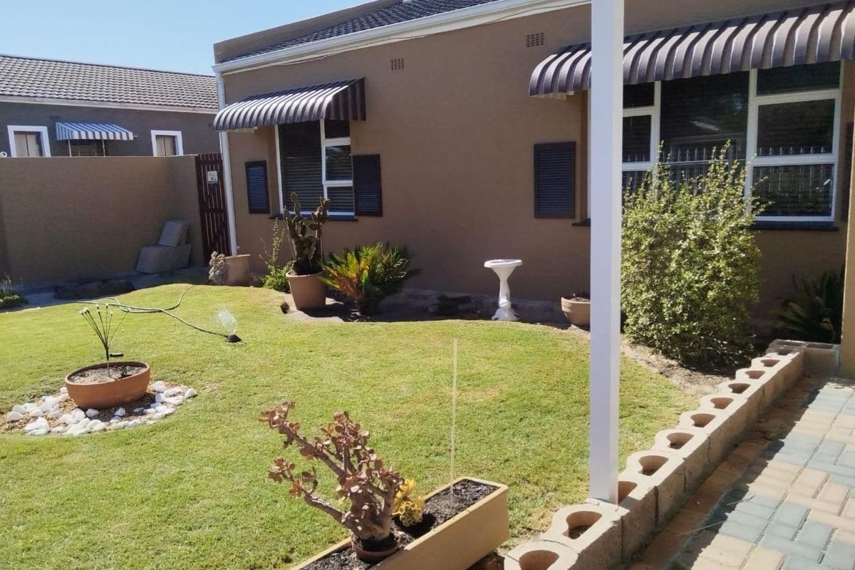A well-maintained rear garden featuring a manicured lawn, paved border, and exterior wall with window awnings.