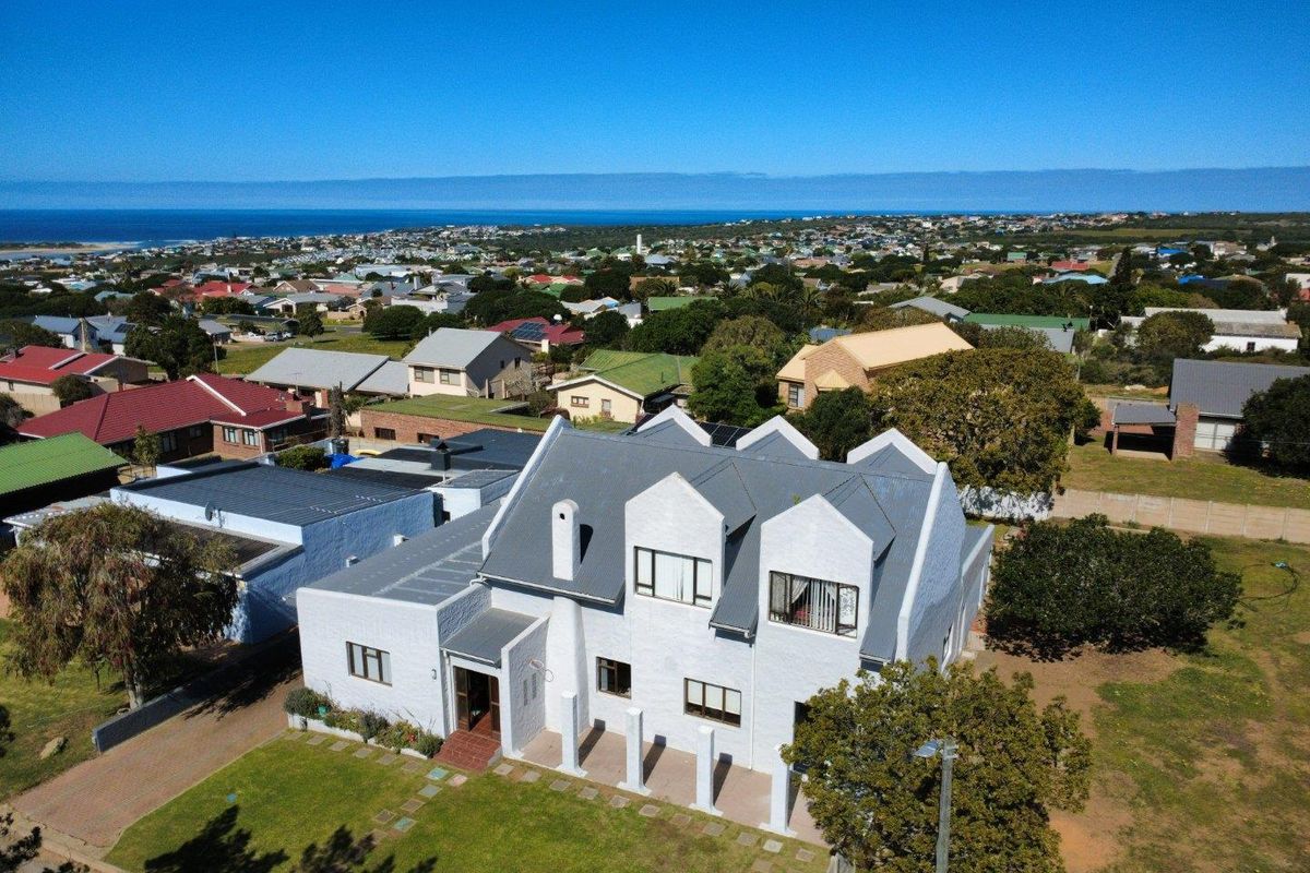 Aerial view of a multi-story residential property featuring a pitched roof, solar panels, and a well-maintained lawn in a coastal neighborhood.