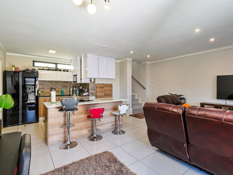 Open-plan living area featuring a modern kitchen with stone countertops, tiled flooring, and a staircase leading to the upper level.