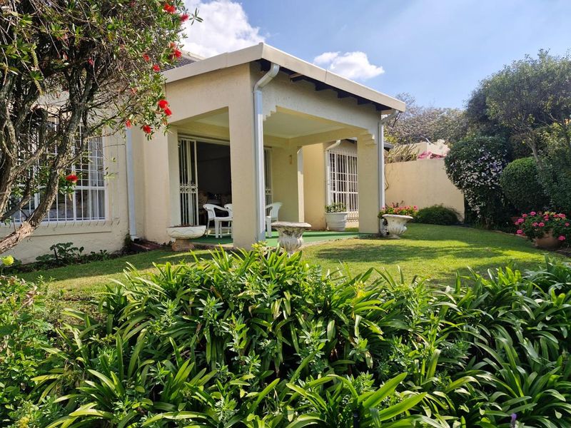 A well-maintained rear exterior view of the townhouse featuring a covered patio, security fixtures, and a lush, established garden.