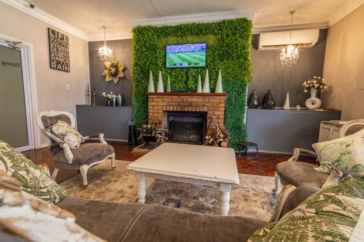 A cozy living room featuring a prominent brick fireplace with a decorative green wall backdrop, parquet flooring, and a wall-mounted air conditioning unit.