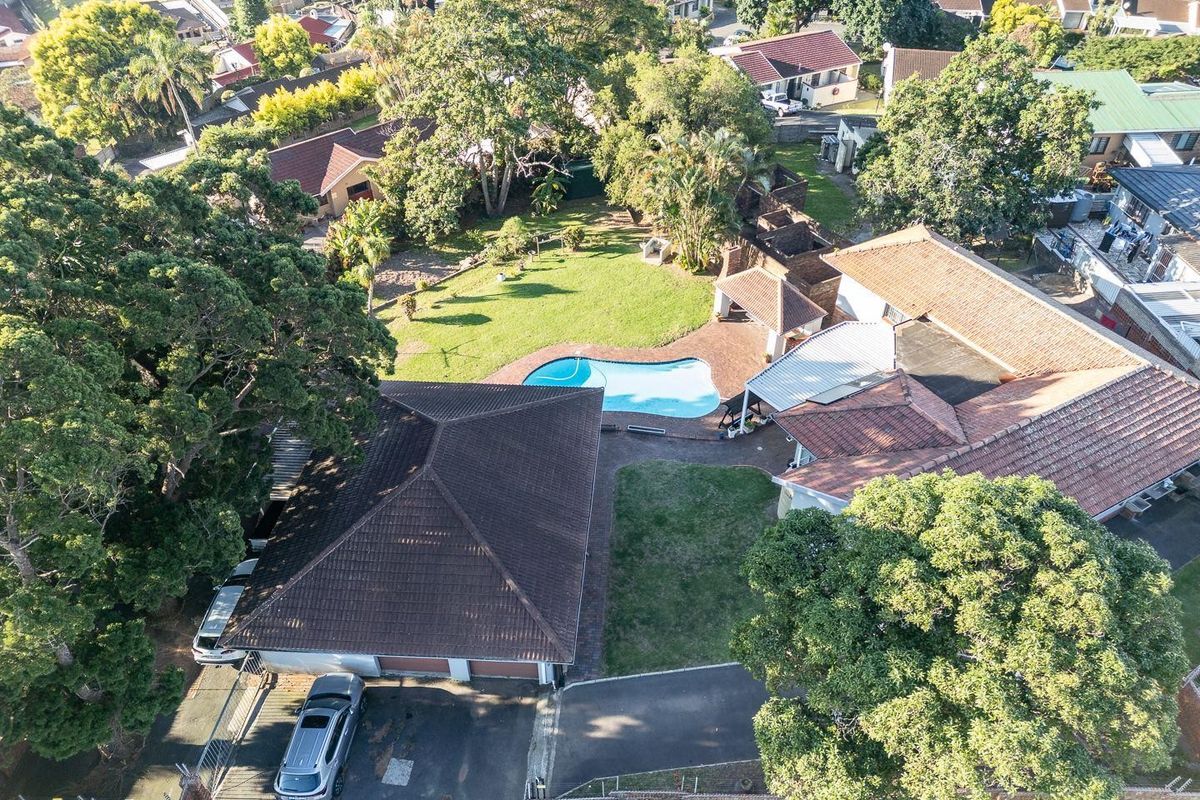 Aerial view of the property featuring a spacious garden, swimming pool, paved driveway, and a detached garage structure.