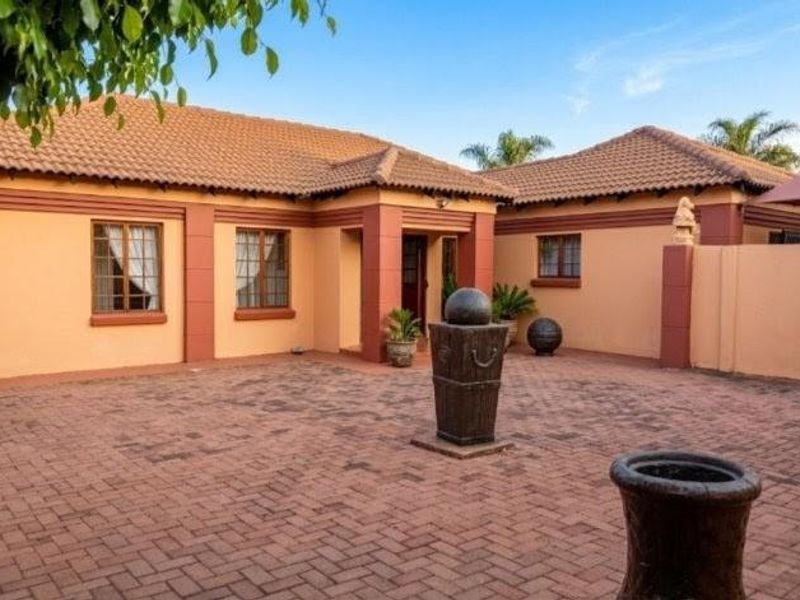 A well-maintained front exterior featuring a paved courtyard, tiled roof, and classic brick facade with secure window treatments.