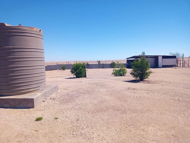 Expansive outdoor area featuring a large water storage tank on a concrete base, perimeter fencing, and a small outbuilding in the distance.