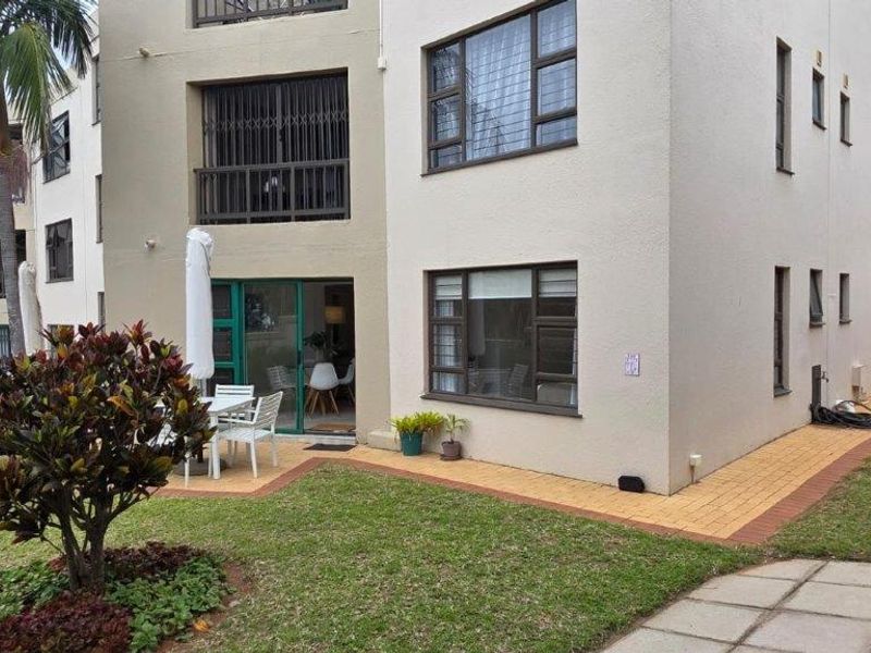 Rear view of the apartment building featuring a private garden, paved walkway, and access to the living area through sliding glass doors.