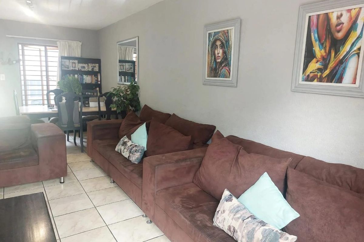 A living room area featuring tiled flooring and a window with security bars, providing a functional space for relaxation.