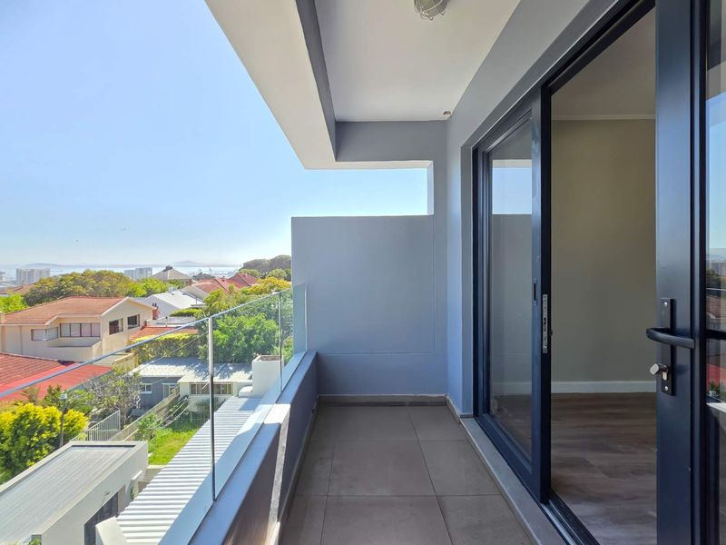 A modern, covered balcony featuring a sleek glass balustrade, tiled flooring, and large sliding doors providing seamless indoor-outdoor flow with neighborhood views.