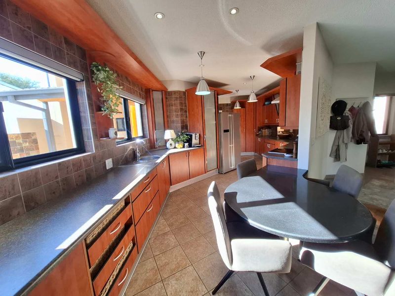 Spacious kitchen featuring cherry wood cabinetry, stone countertops, tiled backsplash, and integrated lighting, with an adjacent dining area.