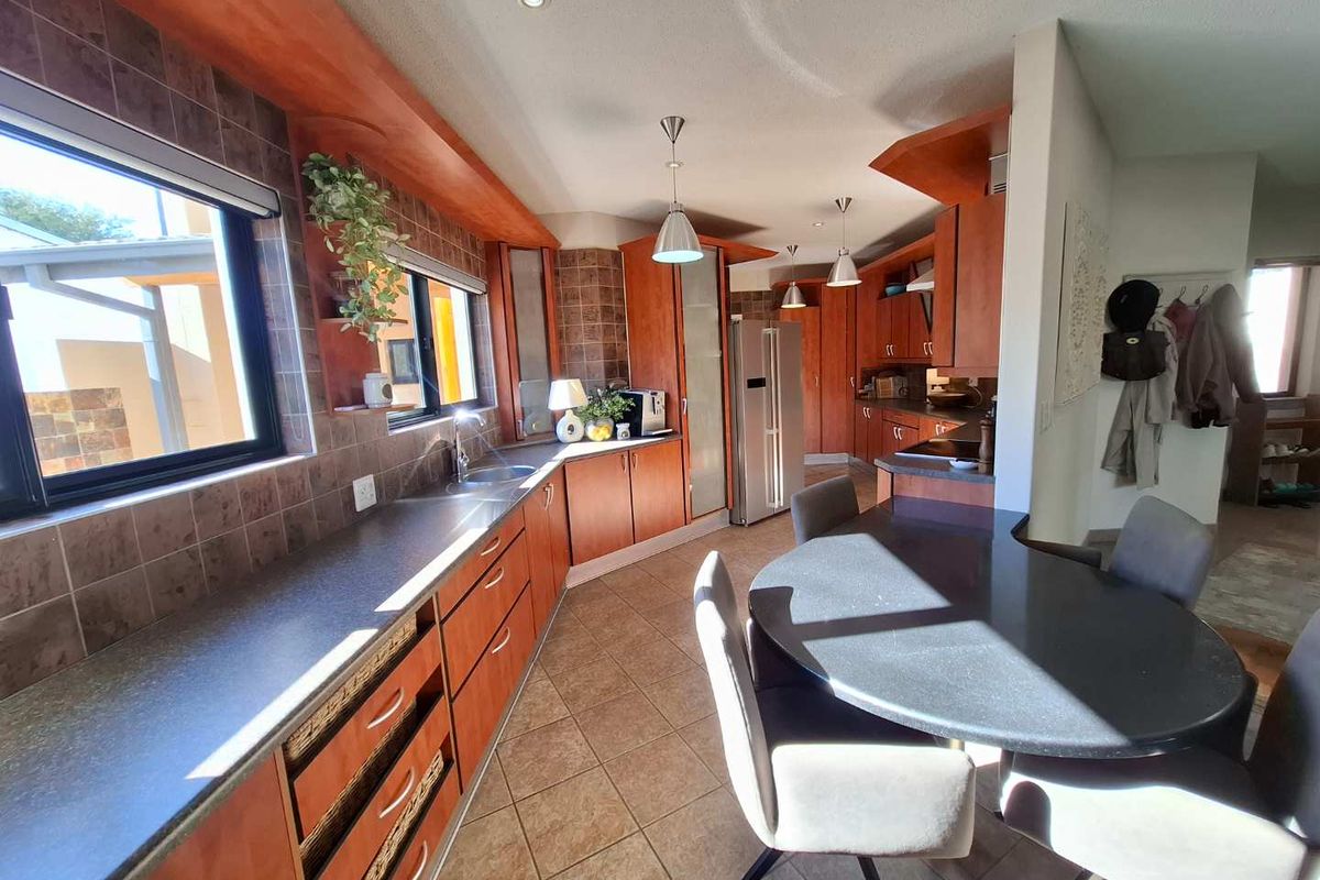Spacious kitchen featuring cherry wood cabinetry, stone countertops, tiled backsplash, and integrated lighting, with an adjacent dining area.