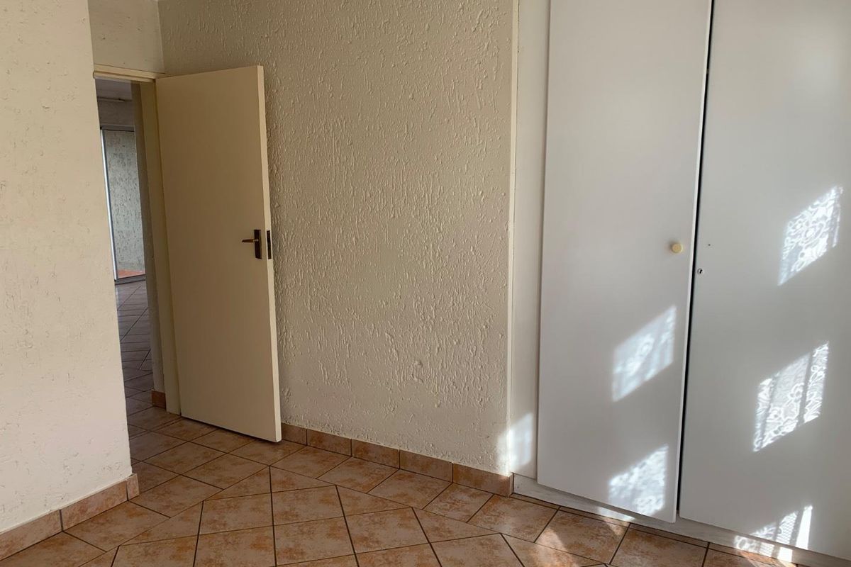A bedroom interior featuring built-in cupboards, tiled flooring, and a doorway leading to an adjacent space.