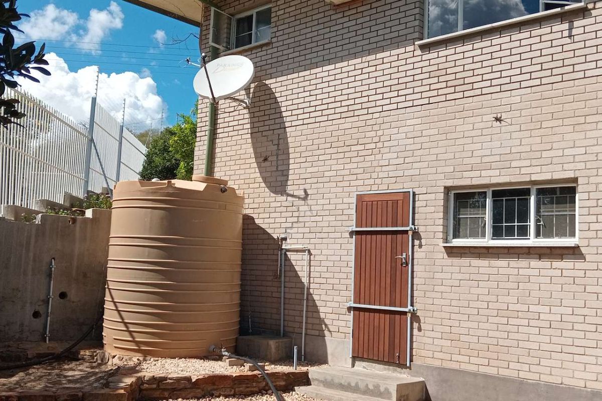 Rear exterior view of the property featuring brick walls, a large water storage tank, security gate, and satellite dish installation.