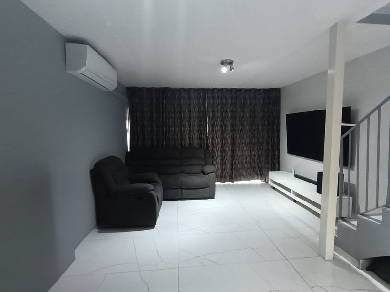A modern living room featuring large format white tiled flooring, a wall-mounted air conditioning unit, and an open staircase with a metal balustrade.