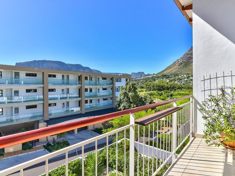 A spacious balcony featuring a metal railing and glass balustrade, offering scenic views of the surrounding landscape and neighbouring apartment complex.