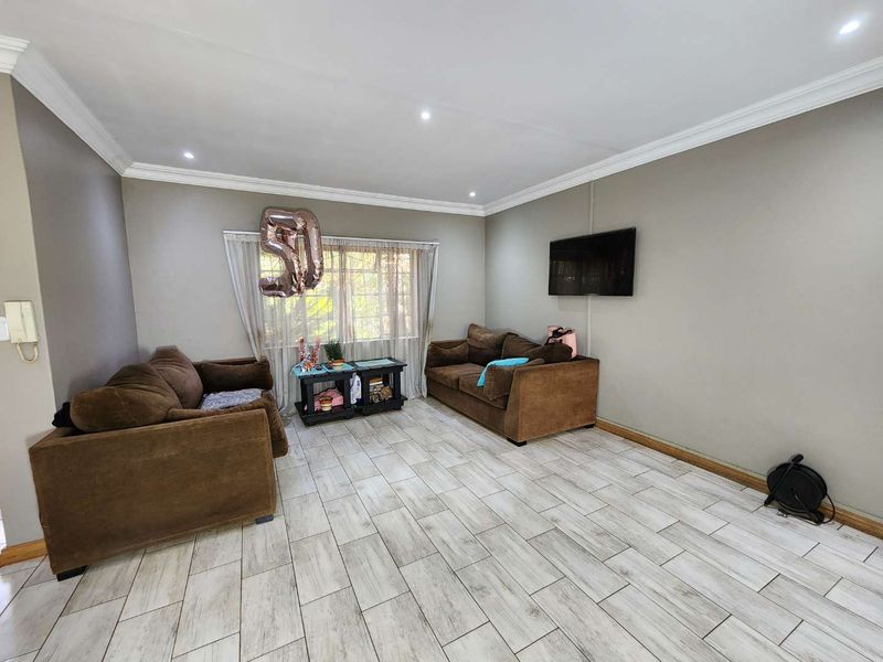 A living room featuring light-toned tiled flooring, crown molding, recessed downlighting, and a wall-mounted television.