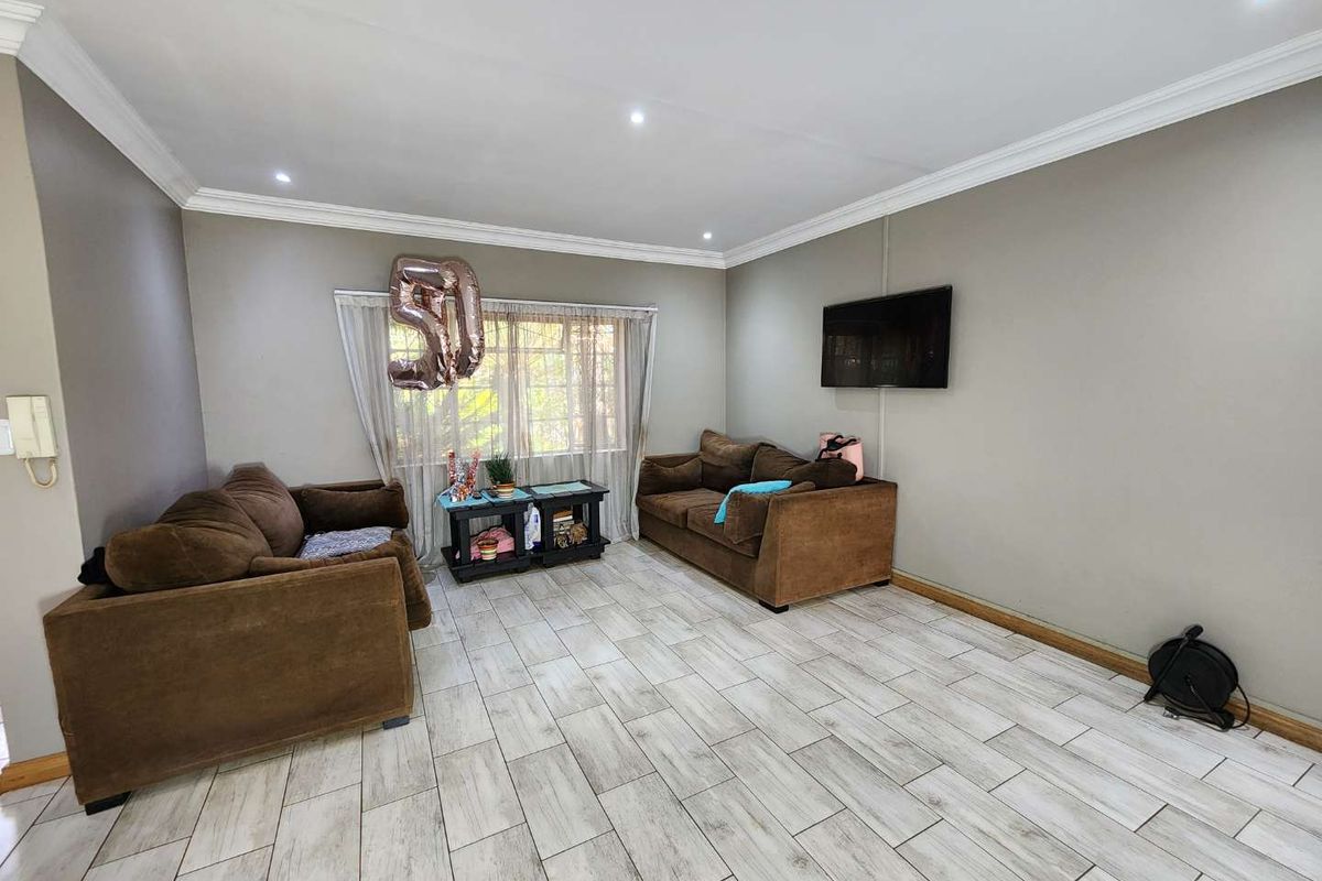 A living room featuring light-toned tiled flooring, crown molding, recessed downlighting, and a wall-mounted television.