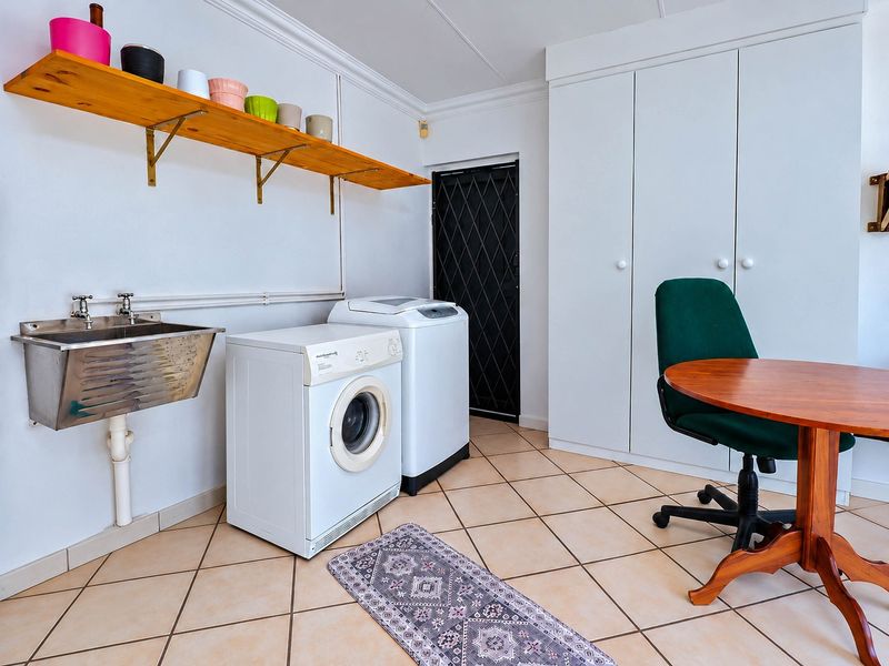 A functional laundry room featuring a stainless steel utility sink, built-in storage cupboards, and tiled flooring, with direct access via a security gate.