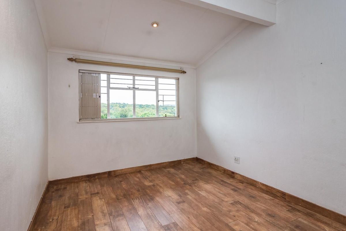 A bright, empty bedroom featuring laminate flooring, a metal-framed window with security bars, and neutral white walls, offering a clean canvas for personalization.