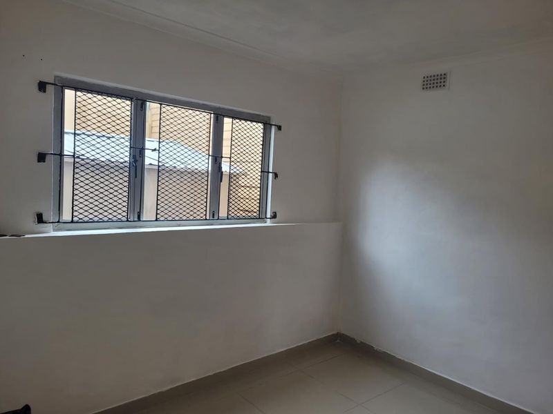 An empty bedroom featuring tiled flooring, a window with security bars, and a ventilation grille, providing a blank canvas for personalization.
