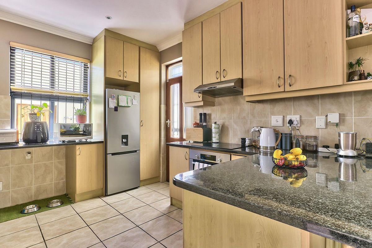 A functional kitchen featuring light wood-tone cabinetry, granite countertops, tiled backsplash, and integrated appliances, offering a practical layout with direct exterior access.