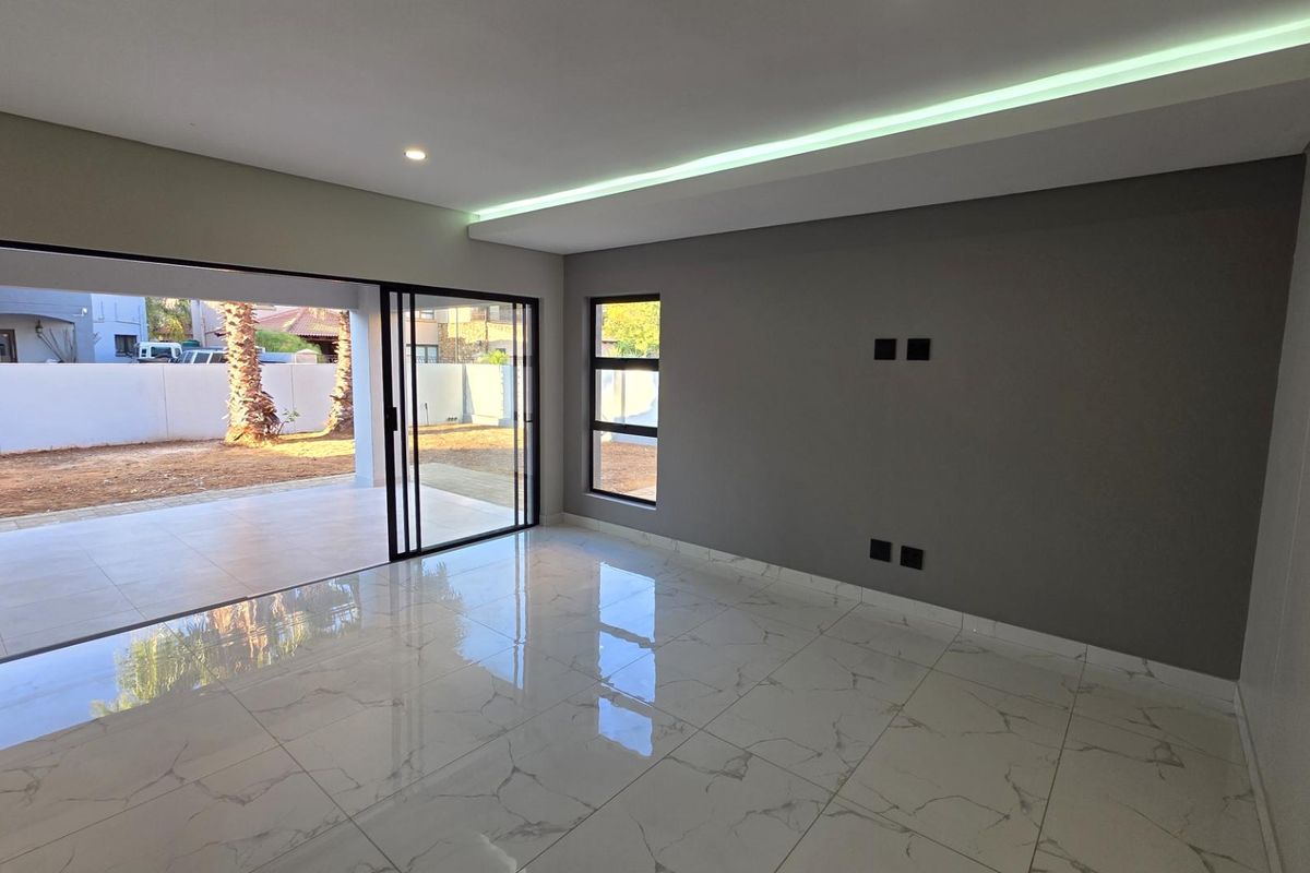 Modern living area featuring large format marble-look floor tiles, recessed LED ceiling lighting, and expansive sliding glass doors opening to a covered patio.