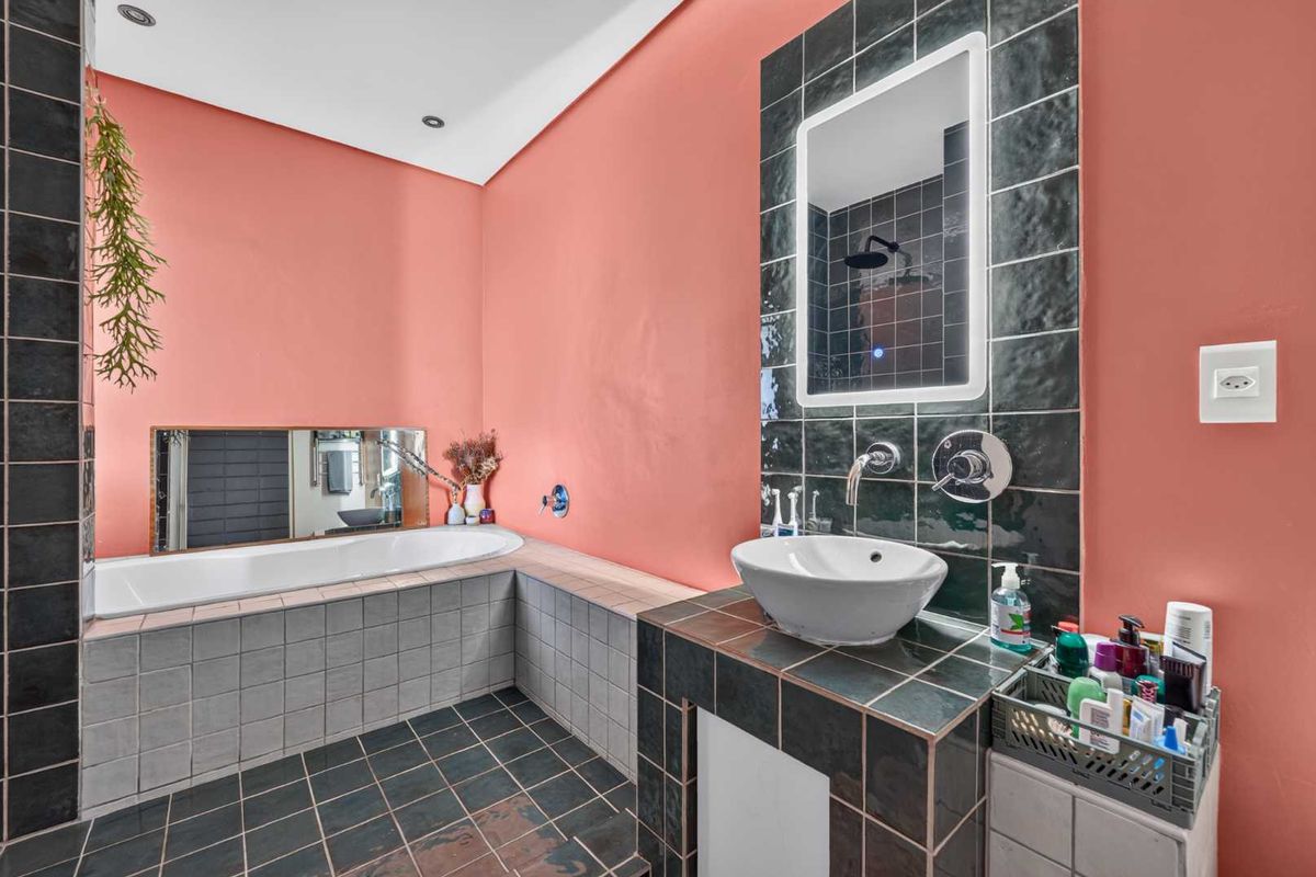 A bathroom featuring a built-in bathtub, a vessel sink on a tiled vanity, and an LED-lit mirror with dark tile accents.
