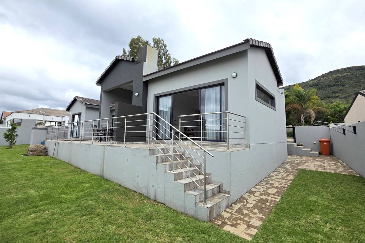 Rear view of the house featuring a raised patio with stainless steel railings, concrete stairs, and sliding glass doors leading to the interior.