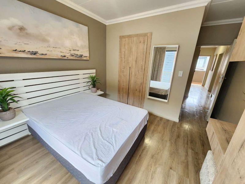 A well-maintained bedroom featuring light wood-look laminate flooring, built-in wardrobe cabinetry, and neutral wall tones, leading into a connecting hallway.